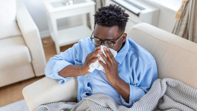 A young man experiencing flu symptoms, taking rest at home.