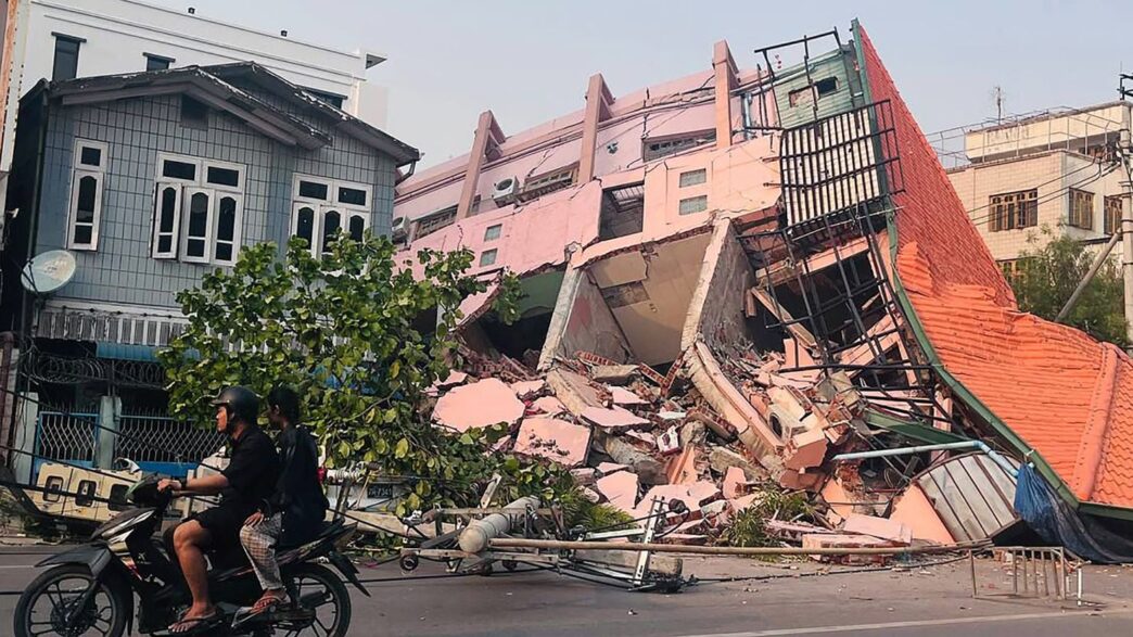 People drive on a motorbike past a collapsed building in Mandalay on March 28, 2025, after an earthquake in central Myanmar. Stringer/AFP/Getty Images