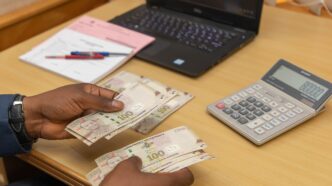 Photo of a hand holding Emalangeni banknotes with a calculator in the background,