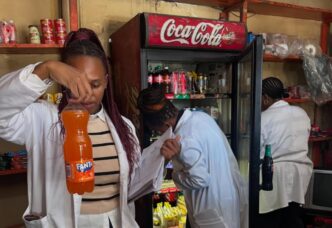 Health inspectors examine the expiry date on a bottled drink during a joint operation in Msunduza, while other officials inspect shelf items for compliance in the background. Photo: Municipal Council Of Mbabane