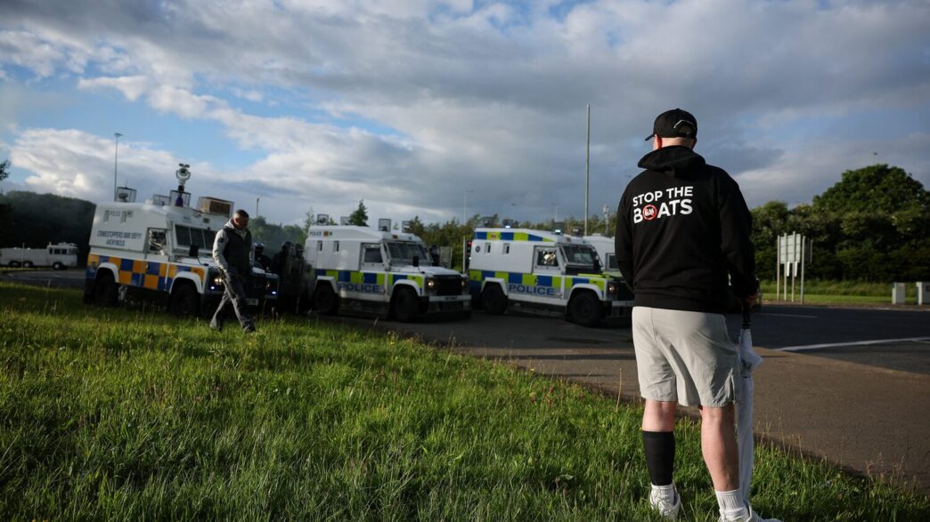 A man wears a 'Stop the Boats' hoody, as police and their vehicles block a road to stop anti-immigrant protesters from reaching Sandyknowes Roundabout, following a knife attack on June 8, which left a man seriously injured and prompted police to declare a critical incident, in Belfast, Northern Ireland, June 10, 2026. REUTERS/Isabel Infantes