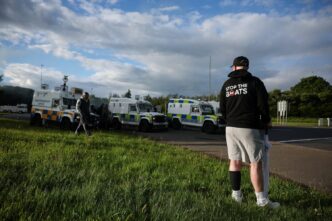 A man wears a 'Stop the Boats' hoody, as police and their vehicles block a road to stop anti-immigrant protesters from reaching Sandyknowes Roundabout, following a knife attack on June 8, which left a man seriously injured and prompted police to declare a critical incident, in Belfast, Northern Ireland, June 10, 2026. REUTERS/Isabel Infantes